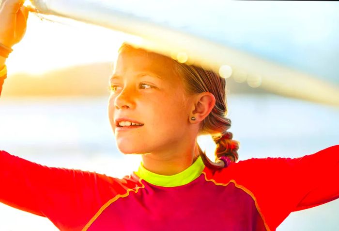 A young girl holds a surfboard high above her head as she walks.