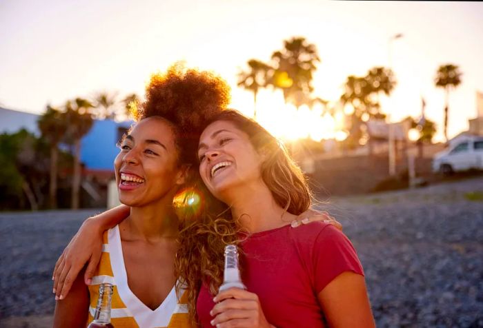 Two cheerful women on the beach, each enjoying a bottle of beer.