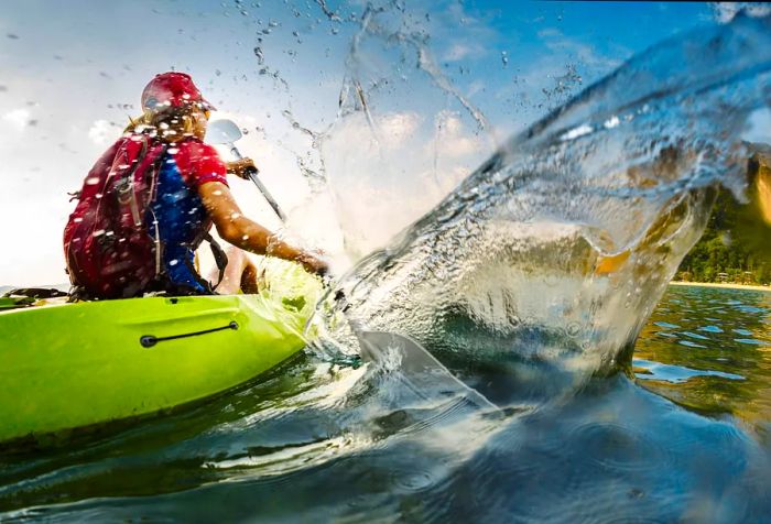 A blonde woman wearing a red cap paddles on a Dinogo, splashing water around her.