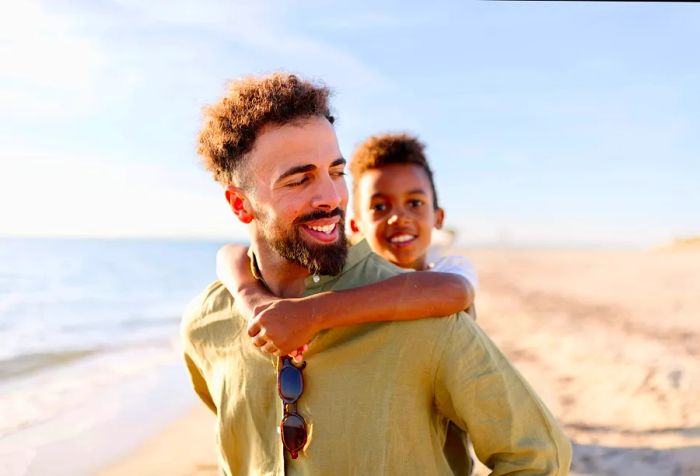 A man carries a small boy on his back as they stroll along the beach.