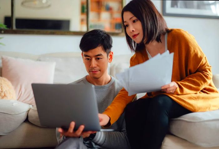 A couple relaxing on a couch in their living room, working on a laptop.