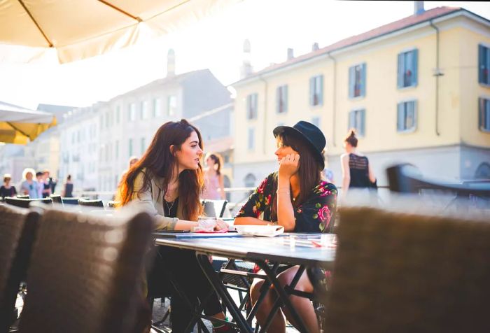 Two female friends share stories while enjoying a meal at an outdoor restaurant.