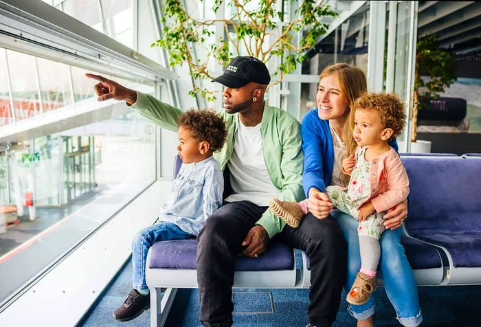 A family spends quality time in an airport lounge, with a parent pointing out something intriguing to the kids as they wait for their flight.