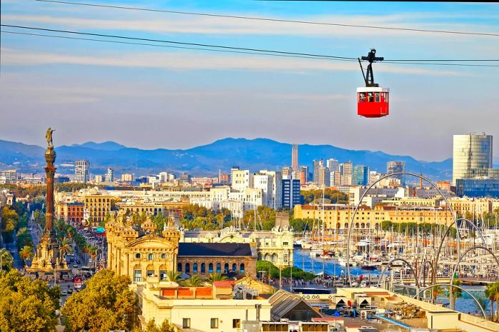 The bright red cabin of the funicular (cable car) stands out against Barcelona's city skyline.