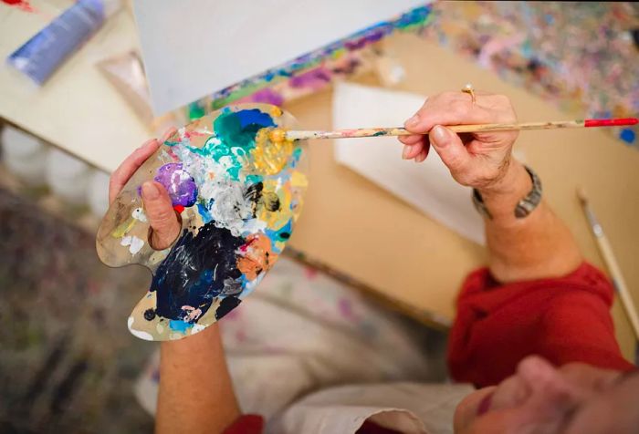 An artist mixing paint with a brush on a wooden palette.