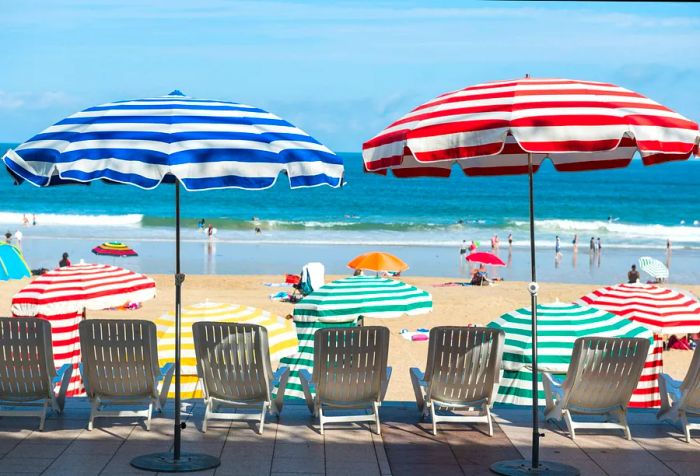 White sun loungers positioned under colorful striped umbrellas, overlooking the sea.