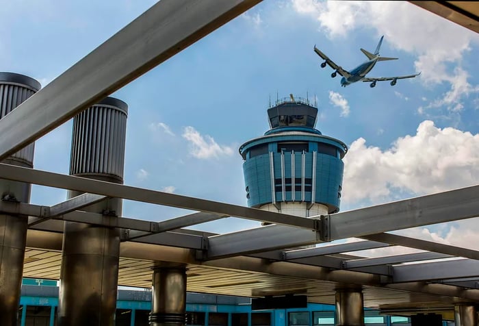 An aircraft soaring above the airport's air traffic control tower.