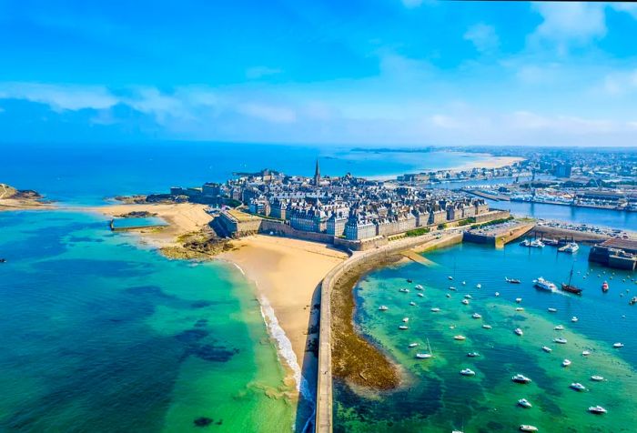 A seawall that divides a beach from the bustling harbor of a coastal city.