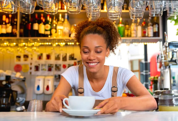 A woman stands at a cafe counter, holding a teacup and saucer.