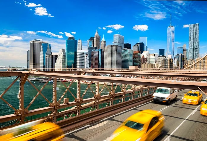 Classic yellow taxis zip across a bridge with a backdrop of the modern coastal city’s towering skyscrapers.