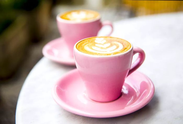 Two pink coffee cups adorned with leaf-shaped designs rest on a table.