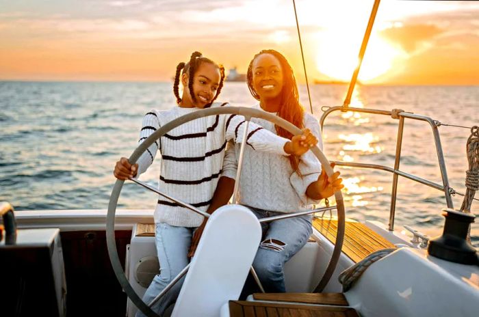 A mother and daughter enjoy sailing in Greece with a picturesque sunset behind them.