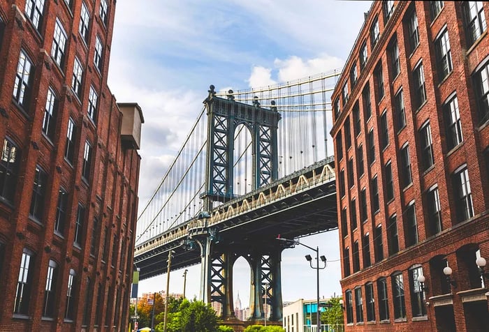 The Manhattan Bridge visible between brownstone warehouse buildings lining the street.