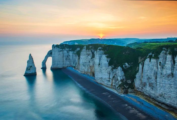 A chalk cliff with an arch along the beach during sunset.