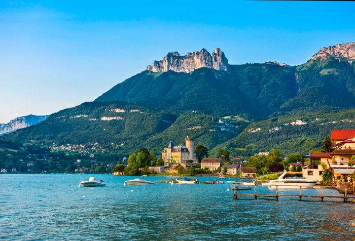 A charming village with chateaus nestled beside a lake, framed by towering mountains.