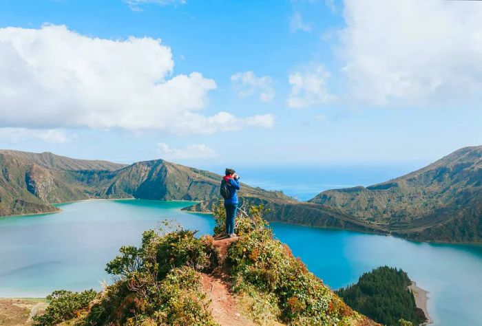 A person captures a stunning photo from a narrow cliff, showcasing a turquoise lake encircled by majestic mountains in the Azores, Portugal.