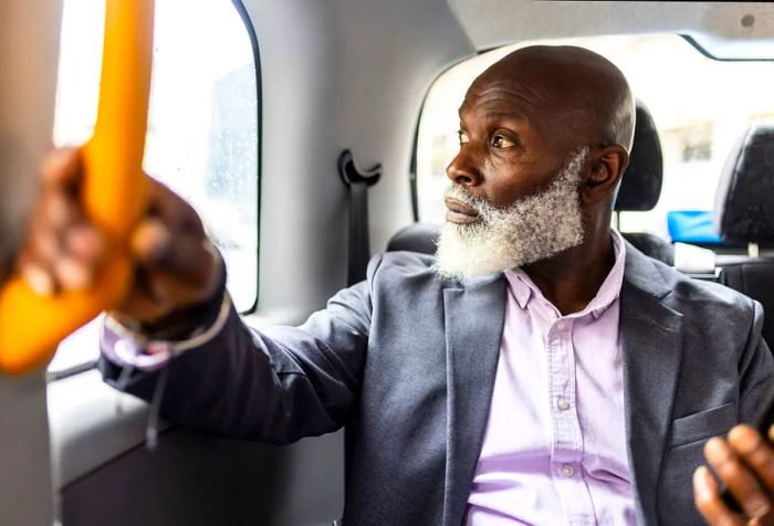 A man with a scruffy white beard gazes out of a car window.