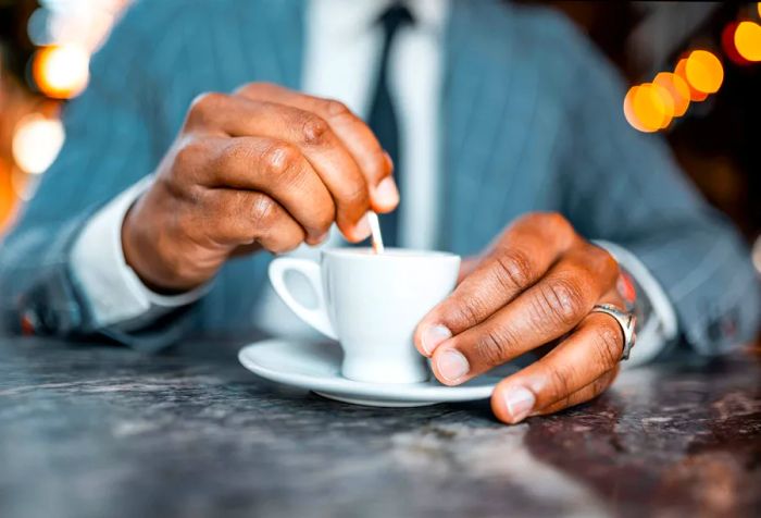 A businessman sits at a table with a small cup of coffee in front of him.