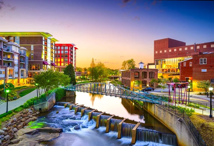 A steel footbridge spans a water canal with a dam, accompanied by a lovely promenade and modern architecture.