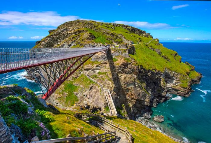 The Tintagel Castle Footbridge gracefully spans the rugged cliffs, hovering above the sparkling waters below.