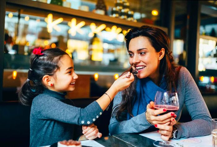 A joyful mother and daughter indulge in a dessert at a restaurant.