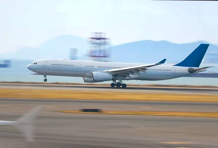 A white airplane touches down on the runway at high speed.