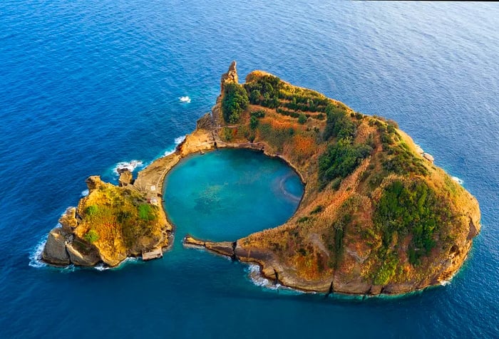 A small island with a protected bay, encircled by rugged, vegetation-covered slopes.