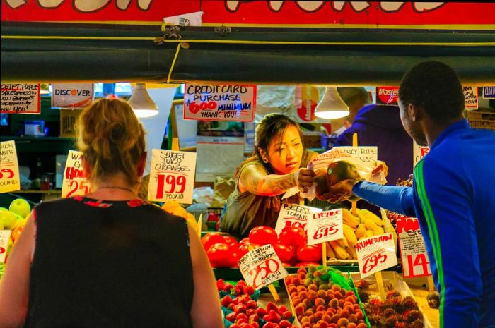 A woman at a market stall hands fresh produce to a customer.