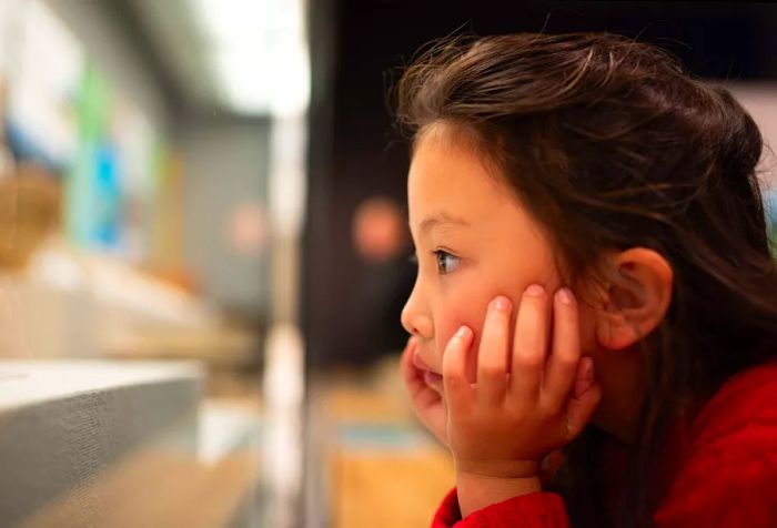 A young girl gazes blankly, resting her head on her hands.