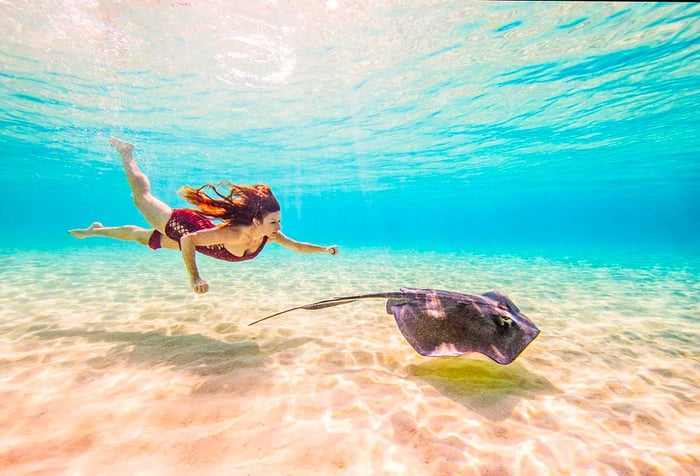 A woman glides gracefully underwater alongside a stingray.