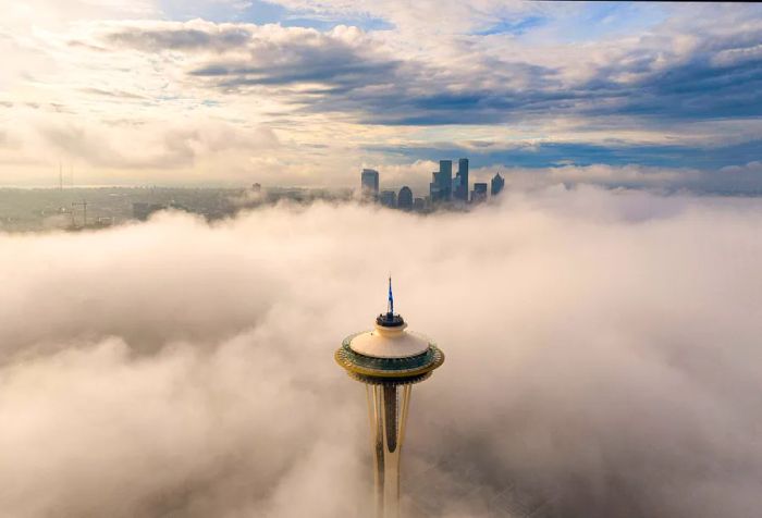 A towering observation structure pierces through the clouds, overlooking a skyline filled with tall buildings in the distance.