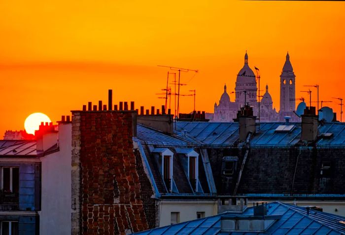 Stunning bell towers and rooftops silhouetted against a warm yellow-orange sunset sky.