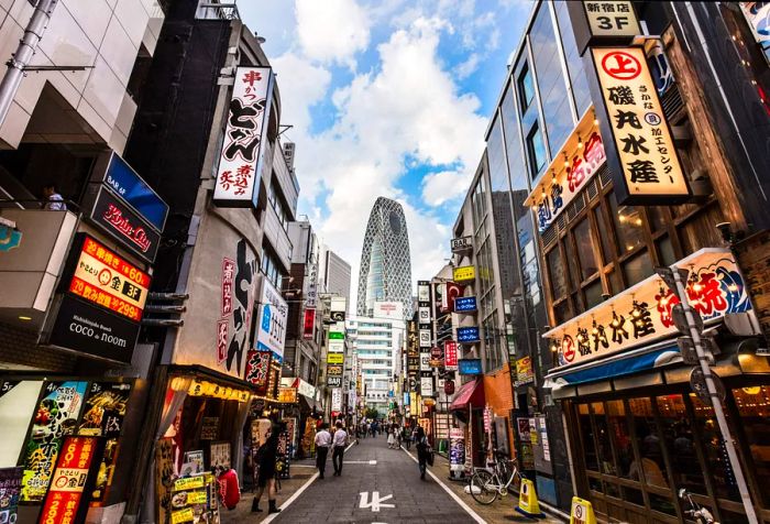 A bustling street filled with shops, illuminated by vibrant LED billboards, with a towering skyscraper in the backdrop.