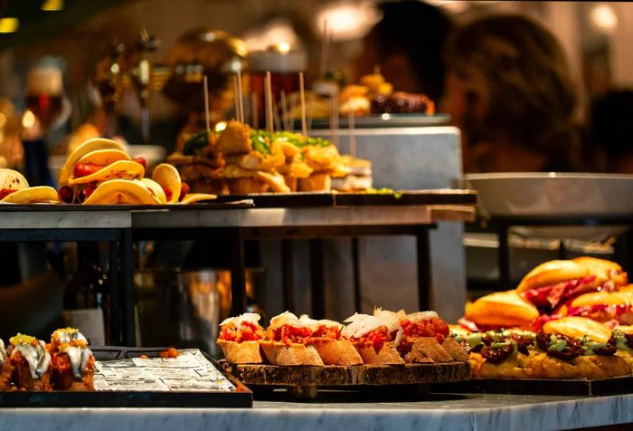 A selection of tapas and pintxos arranged on a buffet table at a bar.
