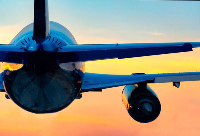 The rear of an airplane soars against a sunset backdrop.