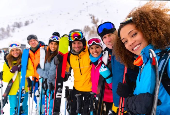 A cheerful group of friends dressed in vibrant winter attire, lined up together with their snowboards.