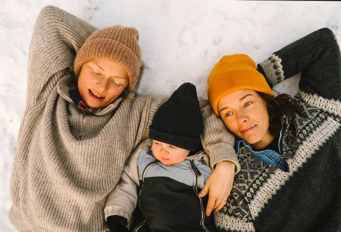 A lesbian LGBTQ couple and their daughter, bundled up in hats, are enjoying a moment together in the snow.