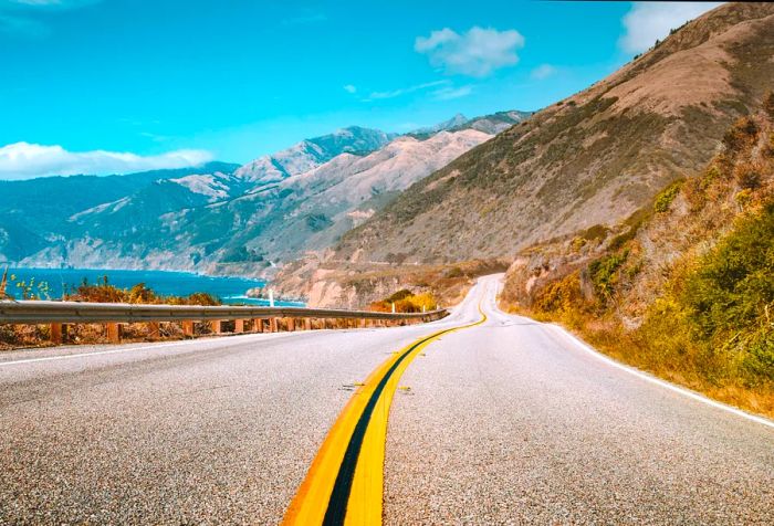 A highway that winds through the base of an enormous mountain range.