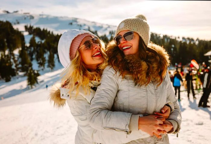 Joyful female couple enjoying winter holiday, embracing on the mountain