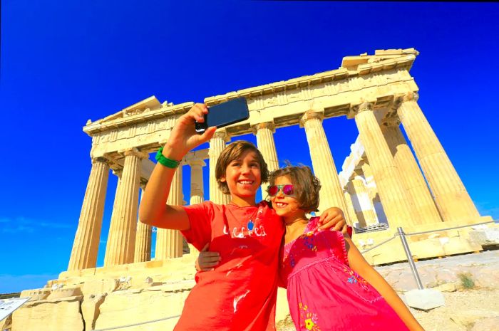 Two kids snapping a selfie in front of the Parthenon in Athens