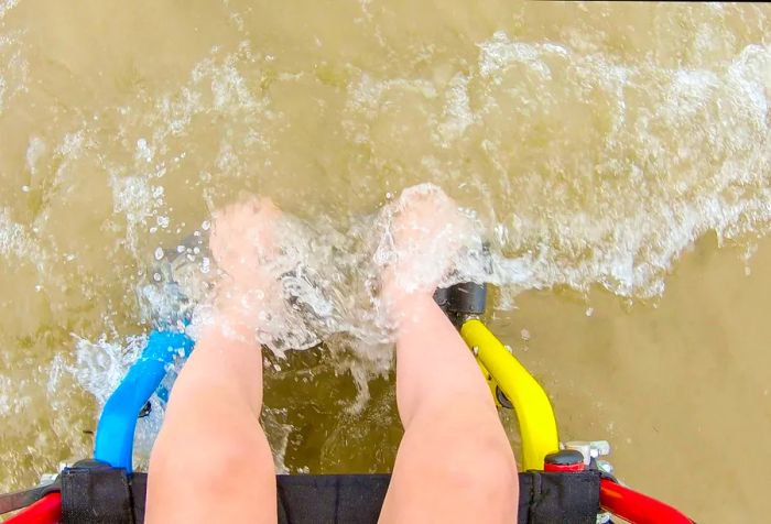 A wheelchair user's feet being gently kissed by the waves.