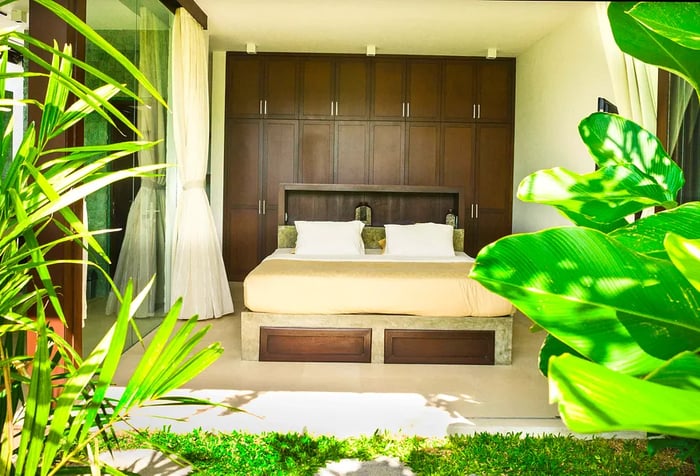 A cozy bed in a room that opens onto a garden filled with lush greenery.