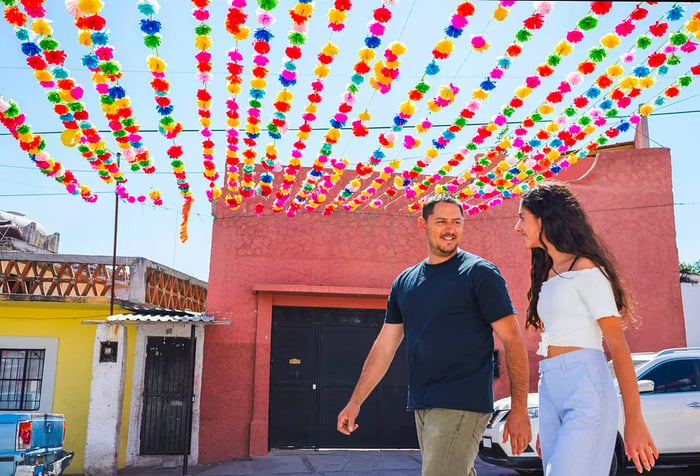 A couple strolling along the street beneath vibrant paper flowers.