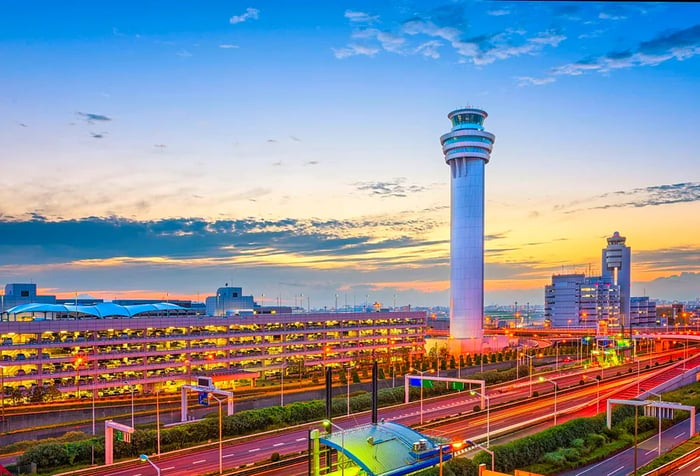 A tall white airport control tower rises toward the picturesque sky, overshadowing the buildings in the foreground.