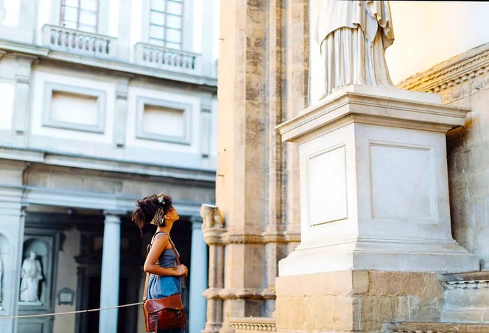 A woman with curly hair secured with a headband gazes up at a white statue.