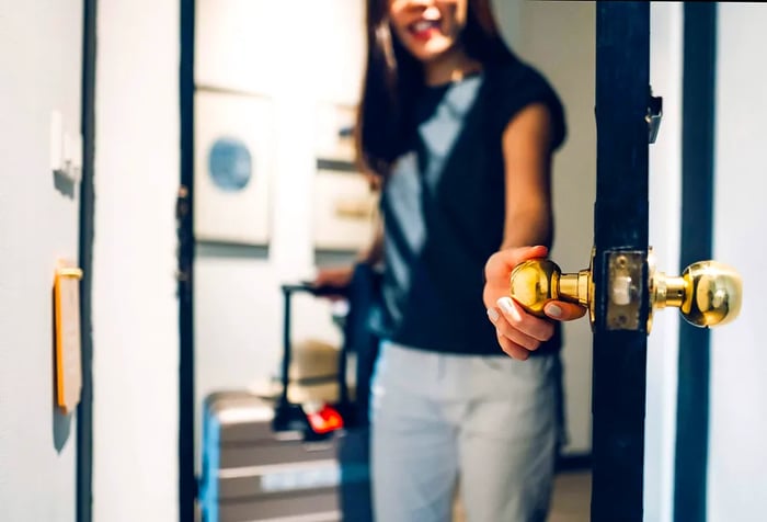 A woman in a black shirt reaches for a door knob to open a room.