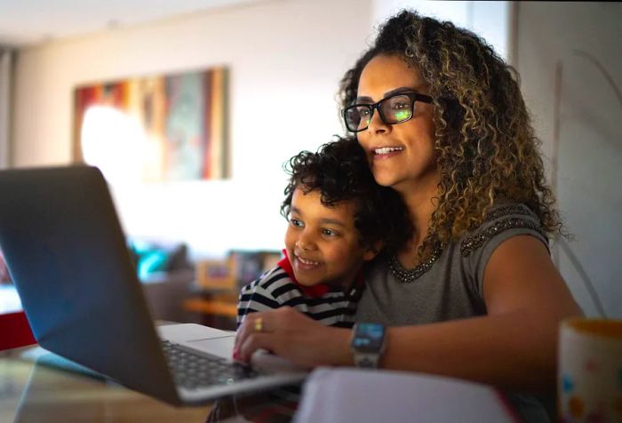 A mother and son at home, browsing on a laptop.