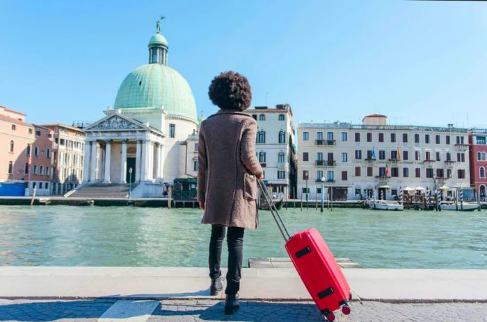 A woman beside a canal with a suitcase in Venice