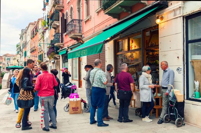 A lively group of people enjoying drinks and conversation outside a wine bar in Venice, Italy