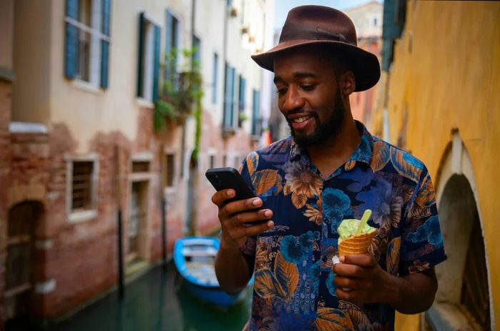 A man enjoying ice cream in one hand and his phone in the other while standing on a bridge in Venice